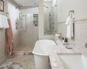 to the right is a dark wood cabinet with a marble top, then a spa like bath tub, then a huge dual shower all with tile floor and half wall